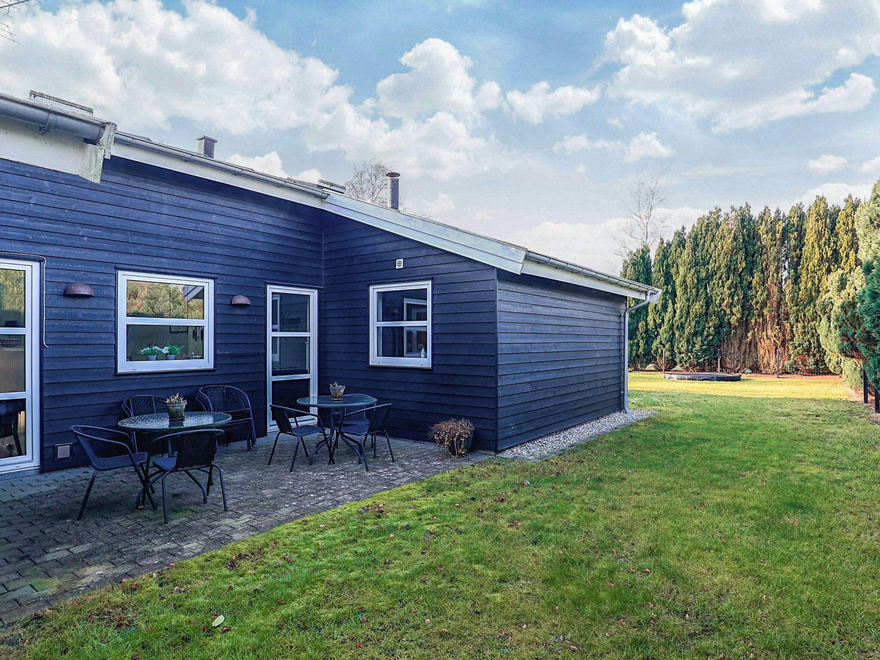 A house with a dark blue exterior, a paved patio with a round table and chairs, and a grassy yard.