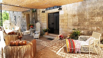 A covered outdoor seating area with wicker furniture and a stone wall backdrop.
