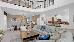 A spacious living room with a large sofa, a coffee table, and a dining area with chairs and a table. - Luxury Contemporary Style House on Storey Lake Resort, Orlando House 6159 (Kissimmee)
