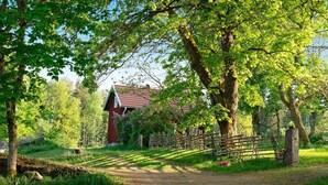 Un sentier rural qui mène à une grange rouge, entourée d’arbres et délimitée par une clôture en bois.