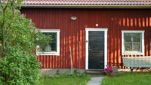 Un bâtiment rouge avec un toit en tuiles, une porte noire et deux fenêtres.