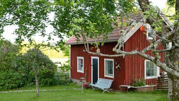 A red wooden house with a sloped roof, a front door, and a small porch area.