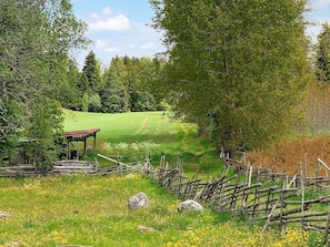 A rural landscape with a wooden structure, possibly a gazebo, surrounded by a fence and a grassy field with yellow flowers. - 4 Star Holiday Home in Nassjo (Nassjo)