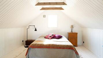 A bedroom with a sloped ceiling, a bed with a patterned bedspread, a nightstand with a lamp, and a window providing natural light.