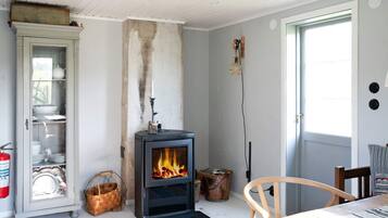 A room with a wood-burning stove, a dining table, a chair, a cabinet with dishes, and a door with a window.
