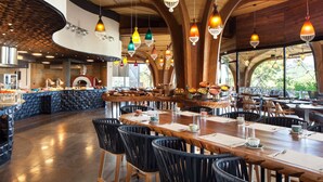 Ein Restaurant mit einer zentralen Bar, mehreren Essplätzen und hängenden Pendelleuchten.