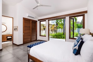 Un dormitorio con cama, ventilador de techo, ventana grande y vista a un jardín.
