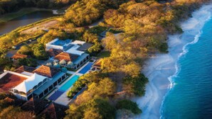 Eine Luftaufnahme eines Küstenresorts mit mehreren Gebäuden, einem Pool und einem Strand.