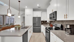 A modern kitchen with white cabinets, a stainless steel refrigerator, a microwave, and a coffee maker. - Rent This Luxury 5 Star House on Champions Gate Resort, Orlando House 6164 (Davenport)