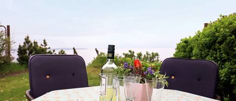 A table set outdoors with a bottle of liquor, glasses, and a vase of flowers.