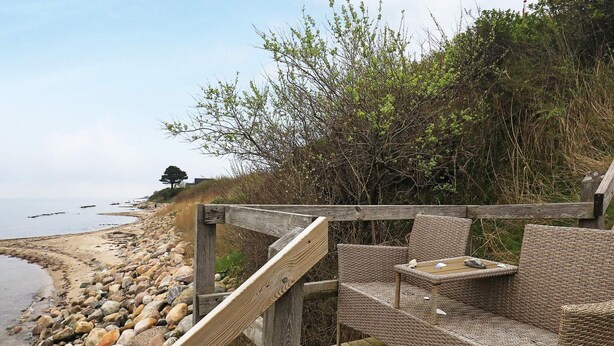 A wooden deck with wicker furniture overlooking a rocky beach. - 6 Person Holiday Home in Brenderup Fyn (Middelfart)