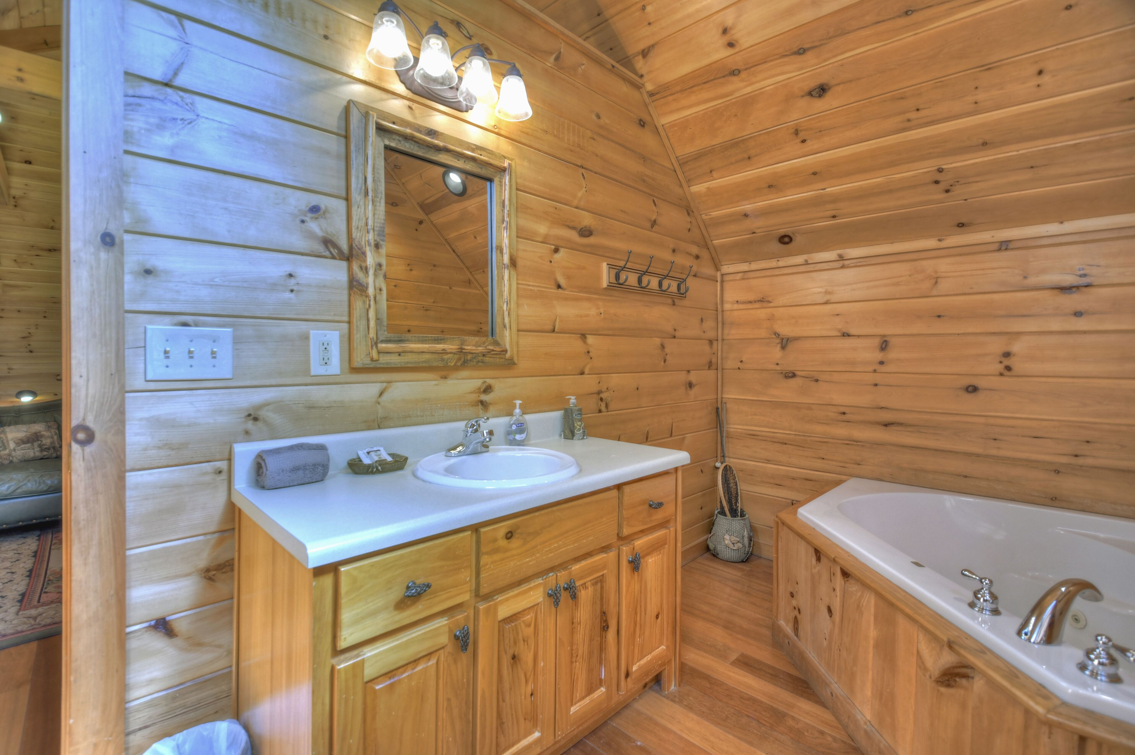 Baño de cabaña de madera con lavamanos, tocador, espejo y bañera.