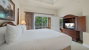 A hotel room with a large bed, a TV, a wooden dresser, a ceiling fan, and a balcony with a view of greenery. - Seven Eagles Orchid: Water Park, Mini-Golf, Golf and More! (Kissimmee)