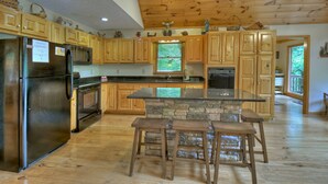 A kitchen with wooden cabinets, a stone island, and a stainless steel refrigerator. - Experience Lakeview Retreat, where pets are pampered by the shimmering waters. Unwind in a hot tub, enjoy WiFi, and  a full game room w/ pool table (Ellijay)