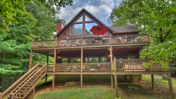 A two-story log cabin with a balcony, wooden deck, and a staircase leading to the upper level. - Experience Lakeview Retreat, where pets are pampered by the shimmering waters. Unwind in a hot tub, enjoy WiFi, and  a full game room w/ pool table (Ellijay)