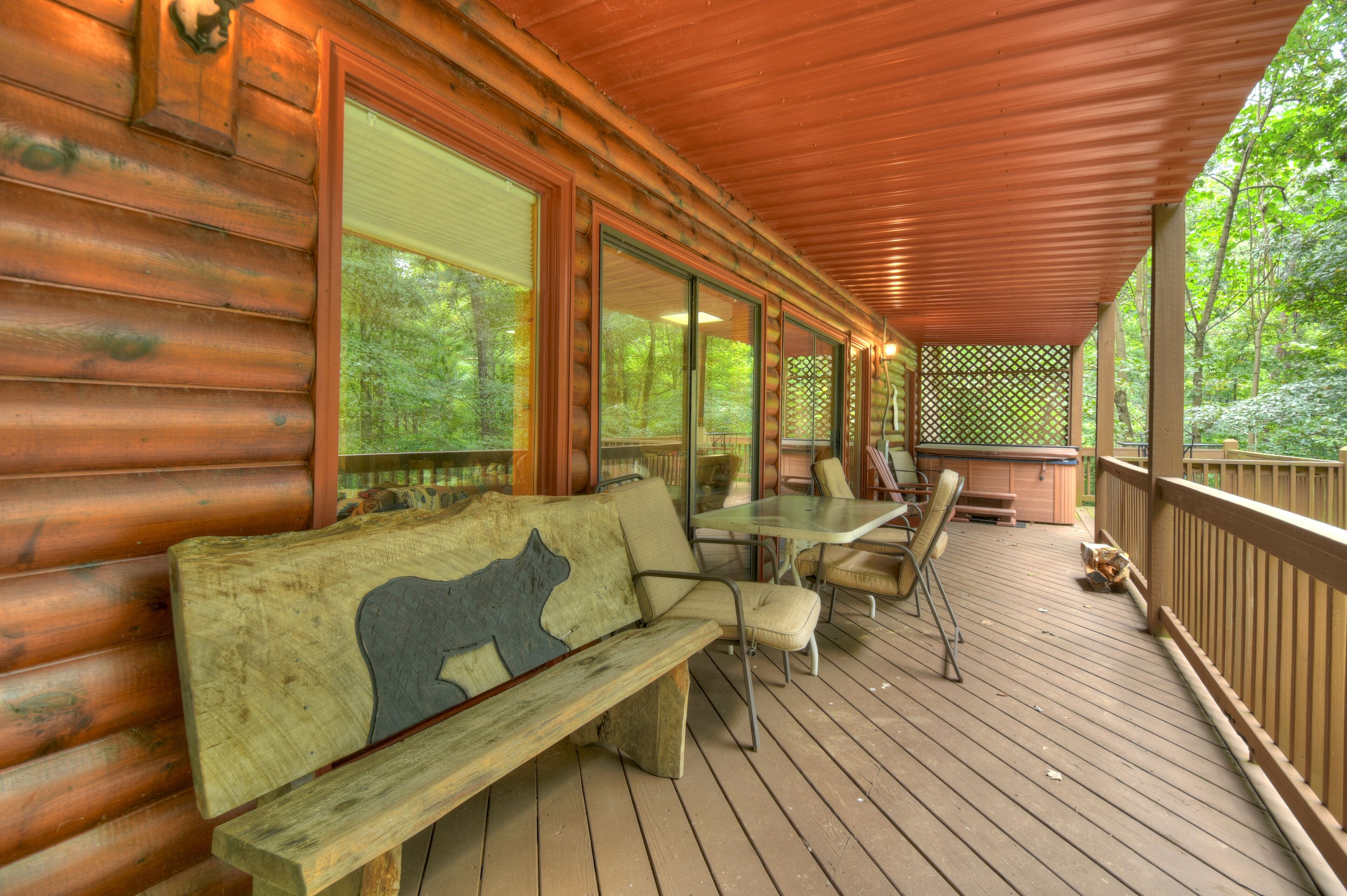 A wooden deck with a bench and chairs, large windows, and a view of the forest.