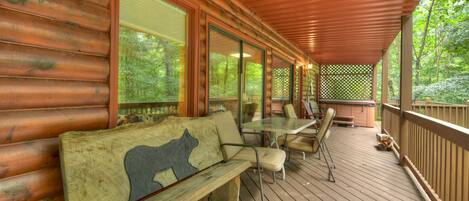 A wooden deck with a bench and chairs, large windows, and a view of the forest.
