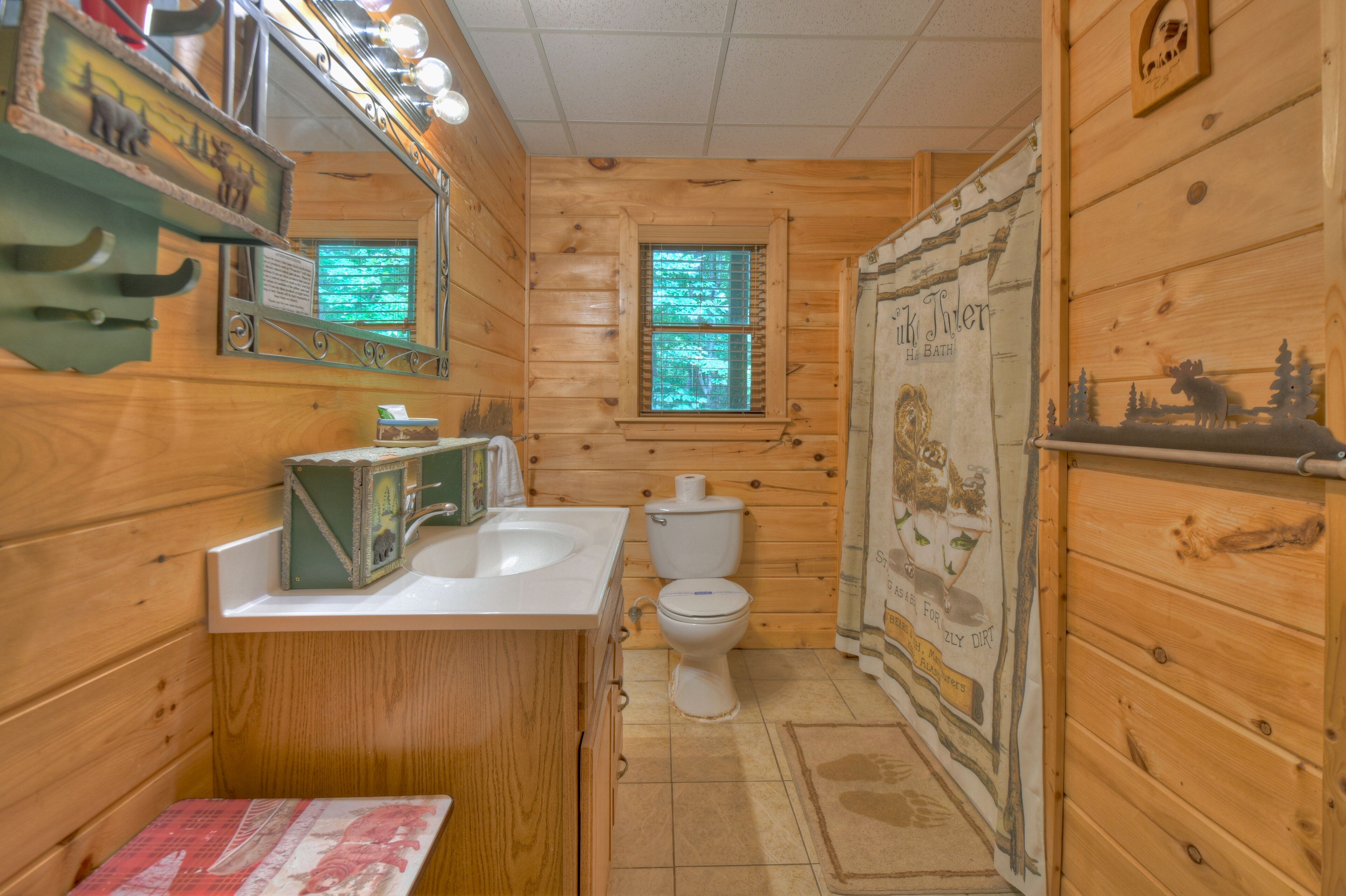 A wooden cabin bathroom with a sink, toilet, and a window with a view of trees.