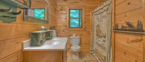A wooden cabin bathroom with a sink, toilet, and a window with a view of trees.