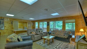 A cozy cabin interior with a fireplace, wooden walls, and large windows offering a view of the outdoors. - Experience Lakeview Retreat, where pets are pampered by the shimmering waters. Unwind in a hot tub, enjoy WiFi, and  a full game room w/ pool table (Ellijay)