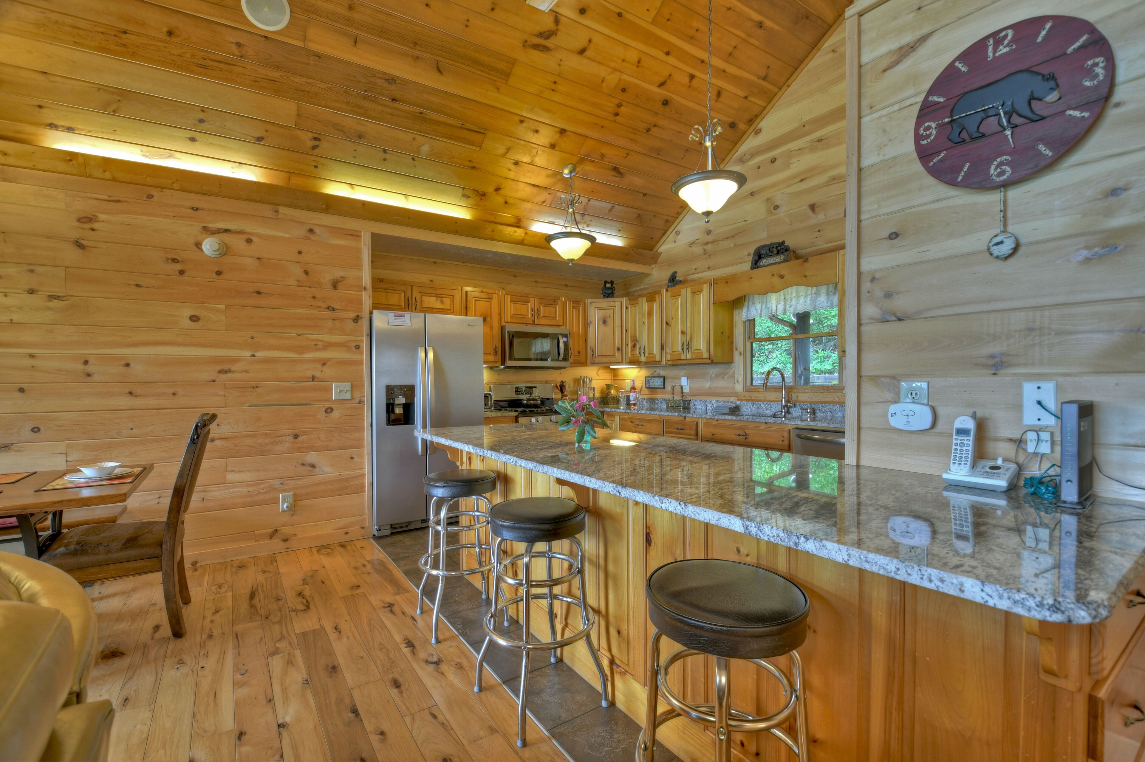 A wooden cabin interior with a kitchen area featuring a refrigerator, microwave, and bar stools.