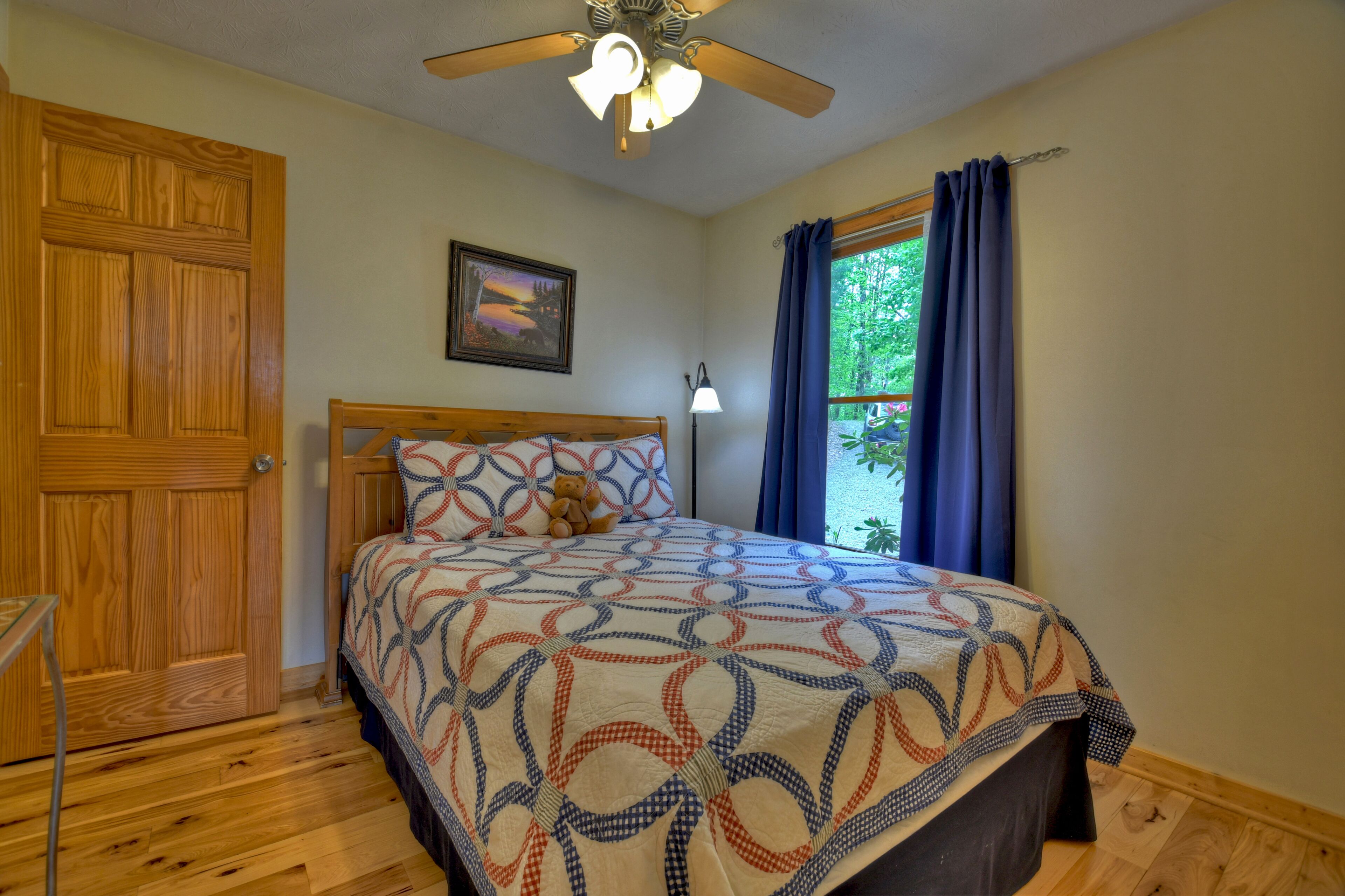 A bedroom with a wooden bed, a ceiling fan, a window with curtains, and a door.