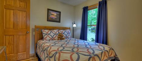 A bedroom with a wooden bed, a ceiling fan, a window with curtains, and a door.