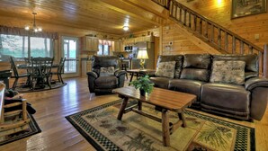 A spacious living room with a wooden staircase, leather furniture, and a dining area with a table and chairs. - Misty Ridge - Where pets are pampered amidst stunning mountain panoramas, with outdoor fireplace, hot tub, firepit, pool table, and WiFi (Ellijay)