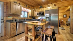 A wooden cabin kitchen with a central island, stainless steel appliances, and a rustic decor. - Misty Ridge - Where pets are pampered amidst stunning mountain panoramas, with outdoor fireplace, hot tub, firepit, pool table, and WiFi (Ellijay)