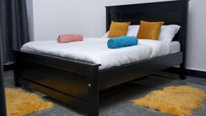 A bed with a black frame, white bedding, and two pillows in yellow and blue. - Peaceful space, with unlimited Wi-Fi internet and free parking at the premises.. (Kampala)