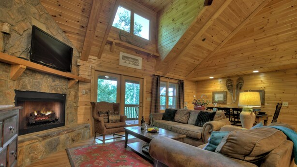 A cozy cabin interior with a stone fireplace, wooden walls, a comfortable sofa, and a television mounted on the wall. - The Retreat is pet-friendly with 3 King beds, Hot Tub, Fire-pit, pool table and minutes from downtown Blue Ridge (Blue Ridge)