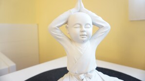 Een witte standbeeld van een figuur in een meditatieve houding.