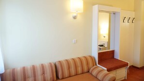 Een kleine, gezellige kamer met een gestreept bankje, een enkele stoel, een witte garderobe en een wandlamp.