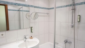 Een badkamer met een wit wastafel, spiegel en douche.