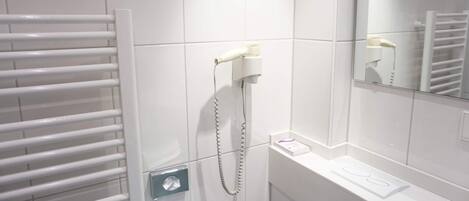 A bathroom with white tiles, a towel rack, a hairdryer, and a mirror.