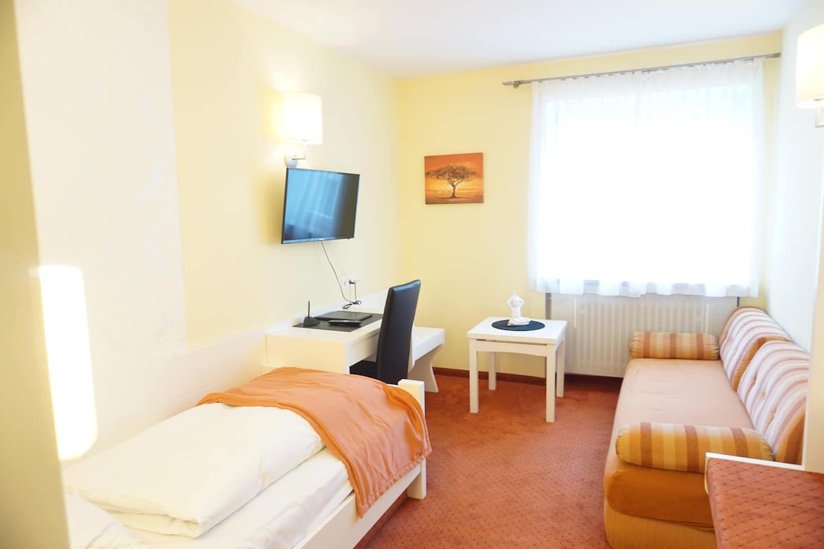 A hotel room with a bed, a desk with a computer, a TV, a small table, and a sofa.