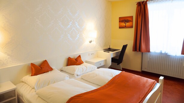 Een hotelkamer met twee bedden, een bureau, een stoel en een schilderij aan de muur.