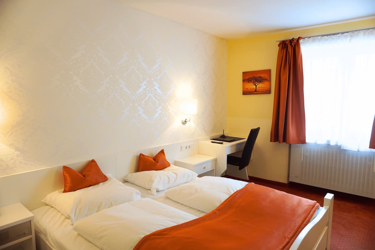 A hotel room with two beds, a desk, a chair, and a painting on the wall.