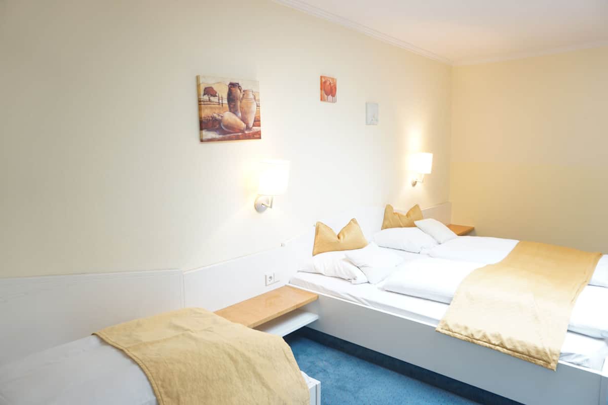 A hotel room with two beds, a small table, and wall-mounted lamps.