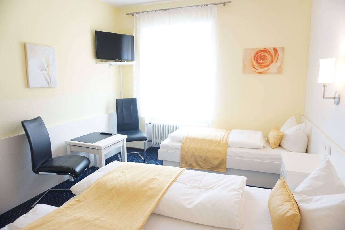 A hotel room with two beds, a desk, a chair, a television, and artwork on the walls.