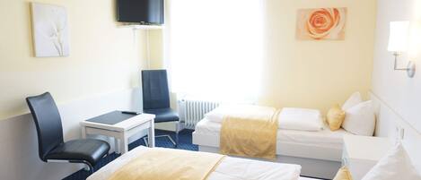 Habitación de hotel con dos camas, un escritorio, una silla, un televisor y obras de arte en las paredes.