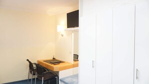 Een compacte, privéruimte met een bureau, twee stoelen, een laptop, een flatscreen-tv en een kledingkast.