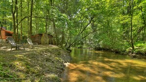 Una cabaña con dos sillas Adirondack junto a un arroyo en un bosque.