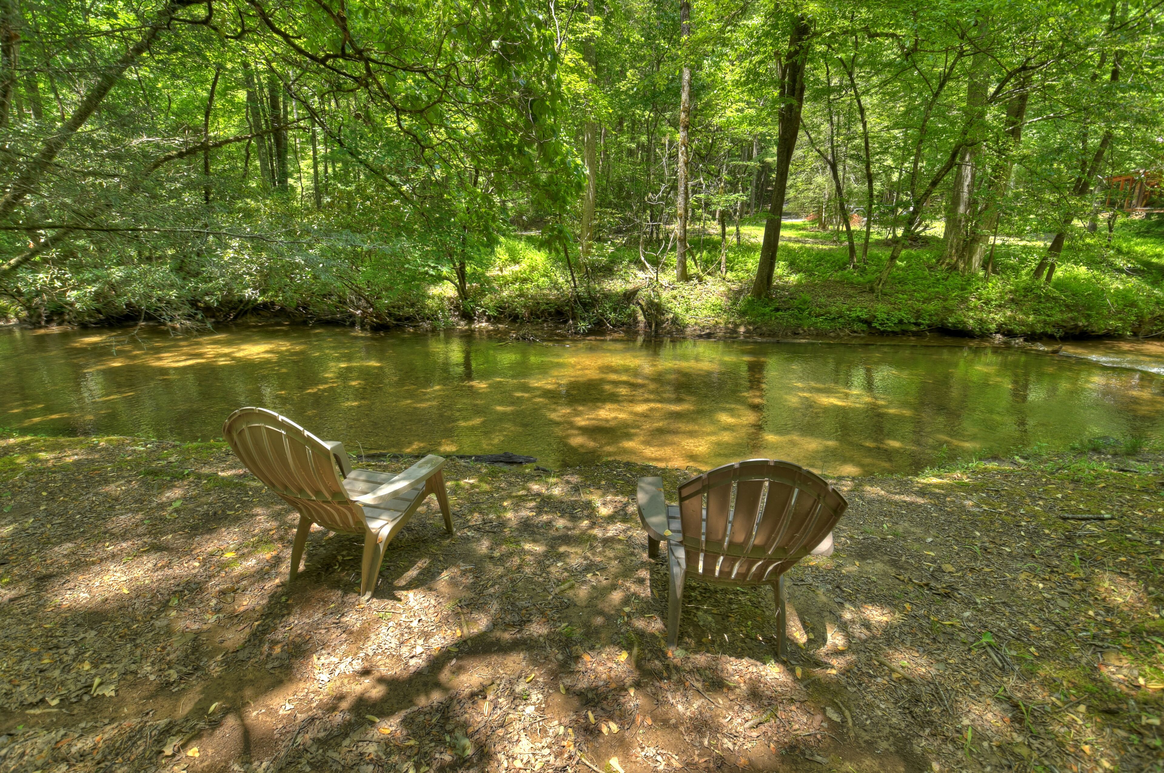 Twee houten stoelen gericht op een rustige rivier in een bebost gebied.