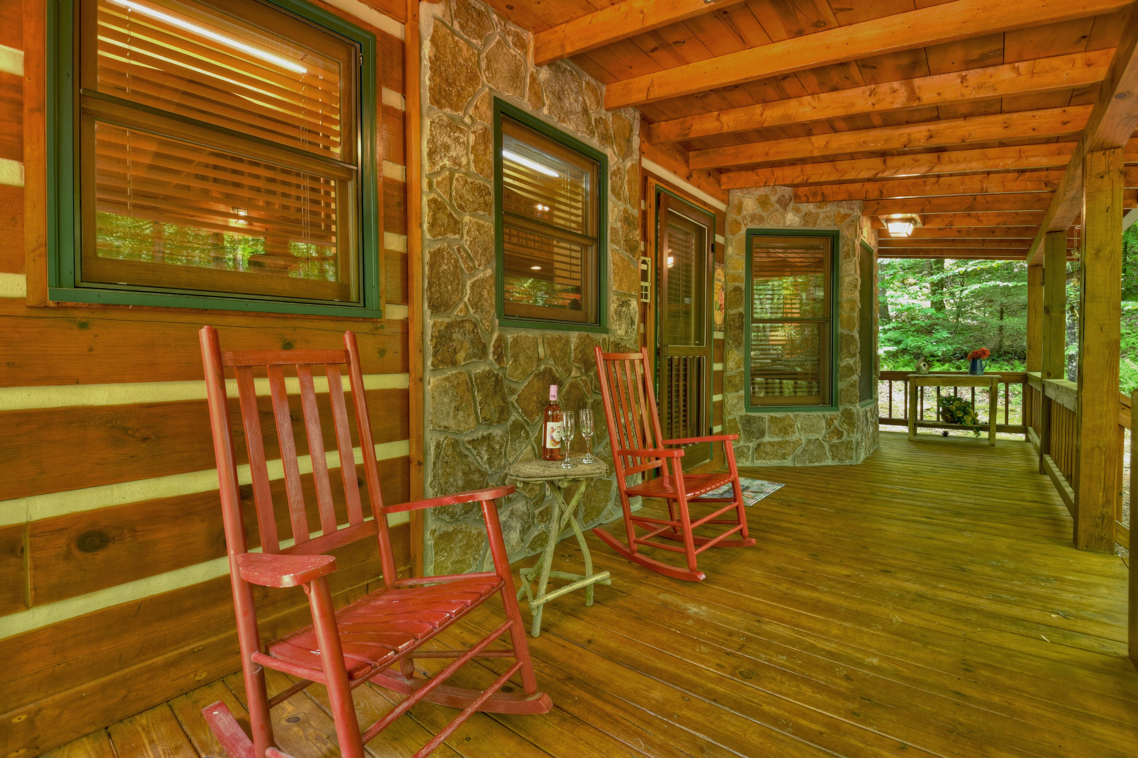 A wooden porch with rocking chairs and a stone wall.