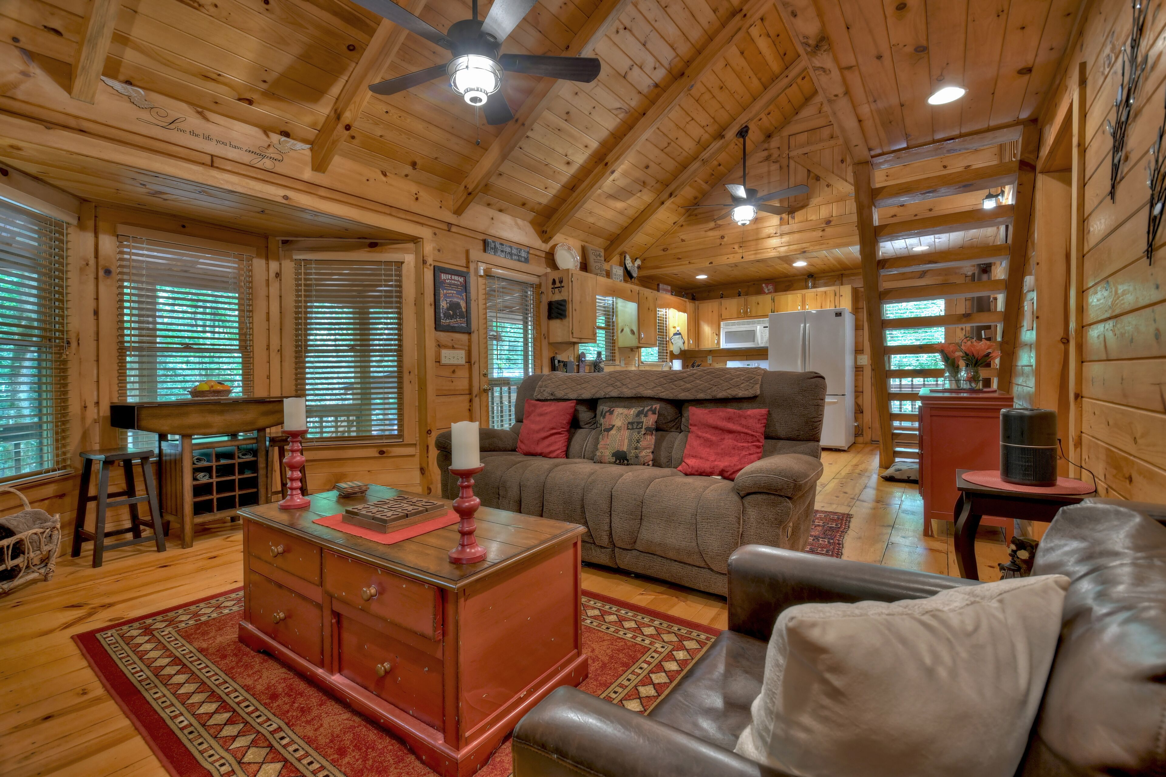 Interior acogedor de una cabaña con techo de madera, una sala de estar con sofá y una mesa de centro, una zona de cocina y un comedor.
