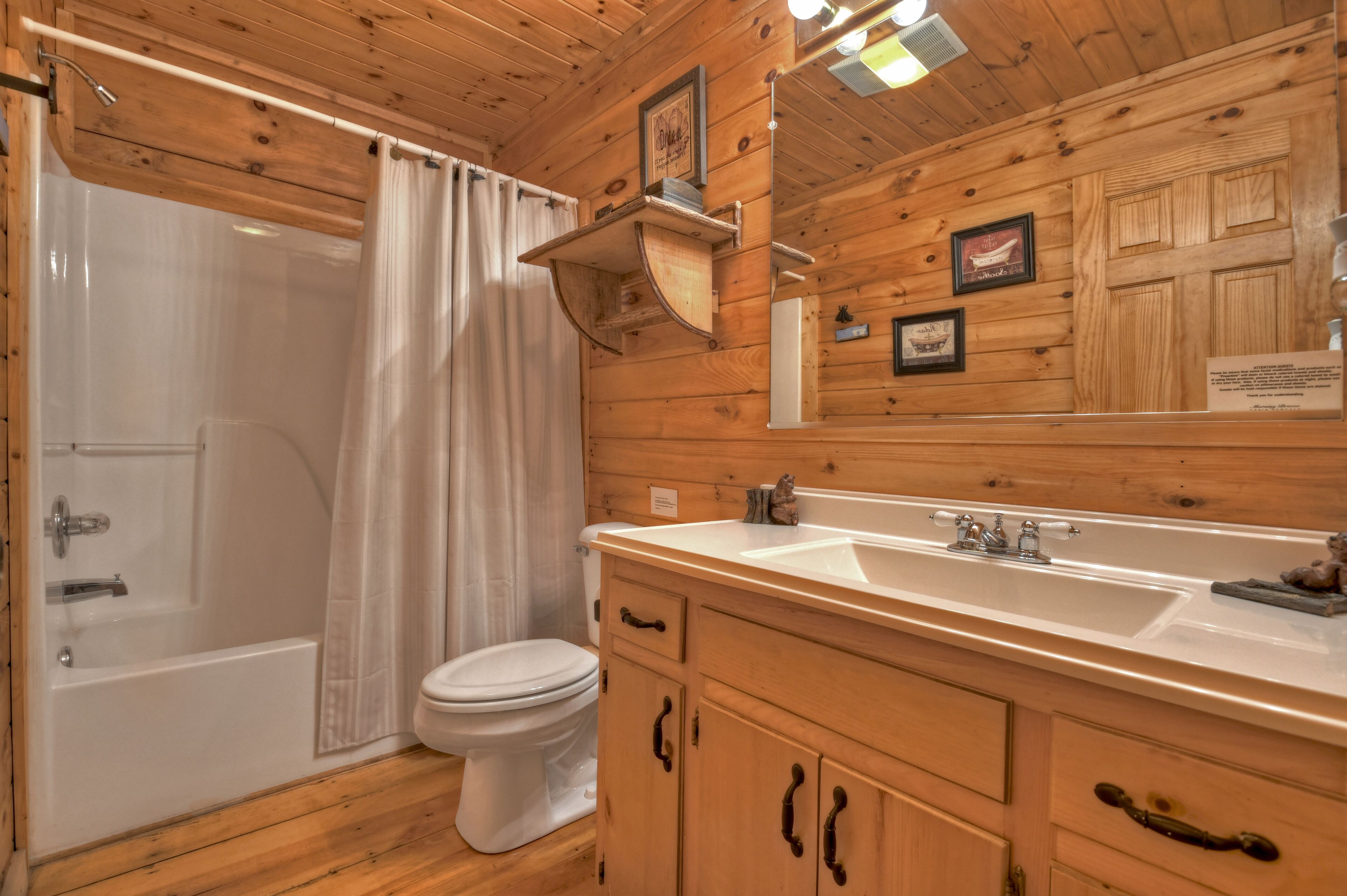 A wooden cabin bathroom with a bathtub, toilet, and a double sink vanity.