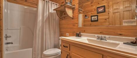 A wooden cabin bathroom with a bathtub, toilet, and a double sink vanity.