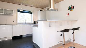 A modern kitchen with white cabinets, a stainless steel range hood, a window, and two bar stools.