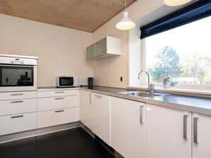 A modern kitchen with white cabinets, a built-in oven, a microwave, and a window with a view of trees. - 4 Person Holiday Home in Oksbol (Oksbol)